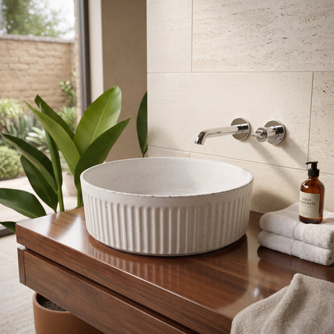 Image of A white ceramic vessel sink with vertical fluting sits on a dark wood vanity in a bathroom setting. A chrome wall-mounted faucet is visible behind it, along with folded white towels and an amber bottle.