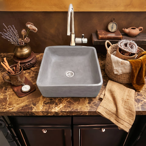 Image of A square gray concrete vessel sink with a chrome gooseneck faucet, set into a brown marble countertop with rustic bathroom accessories.