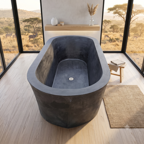 Image of A freestanding rectangular bathtub with a dark charcoal concrete finish, positioned in a modern bathroom with large windows overlooking an African savanna landscape. A small wooden stool with books sits to the right of the tub, and a woven rug is on the floor.